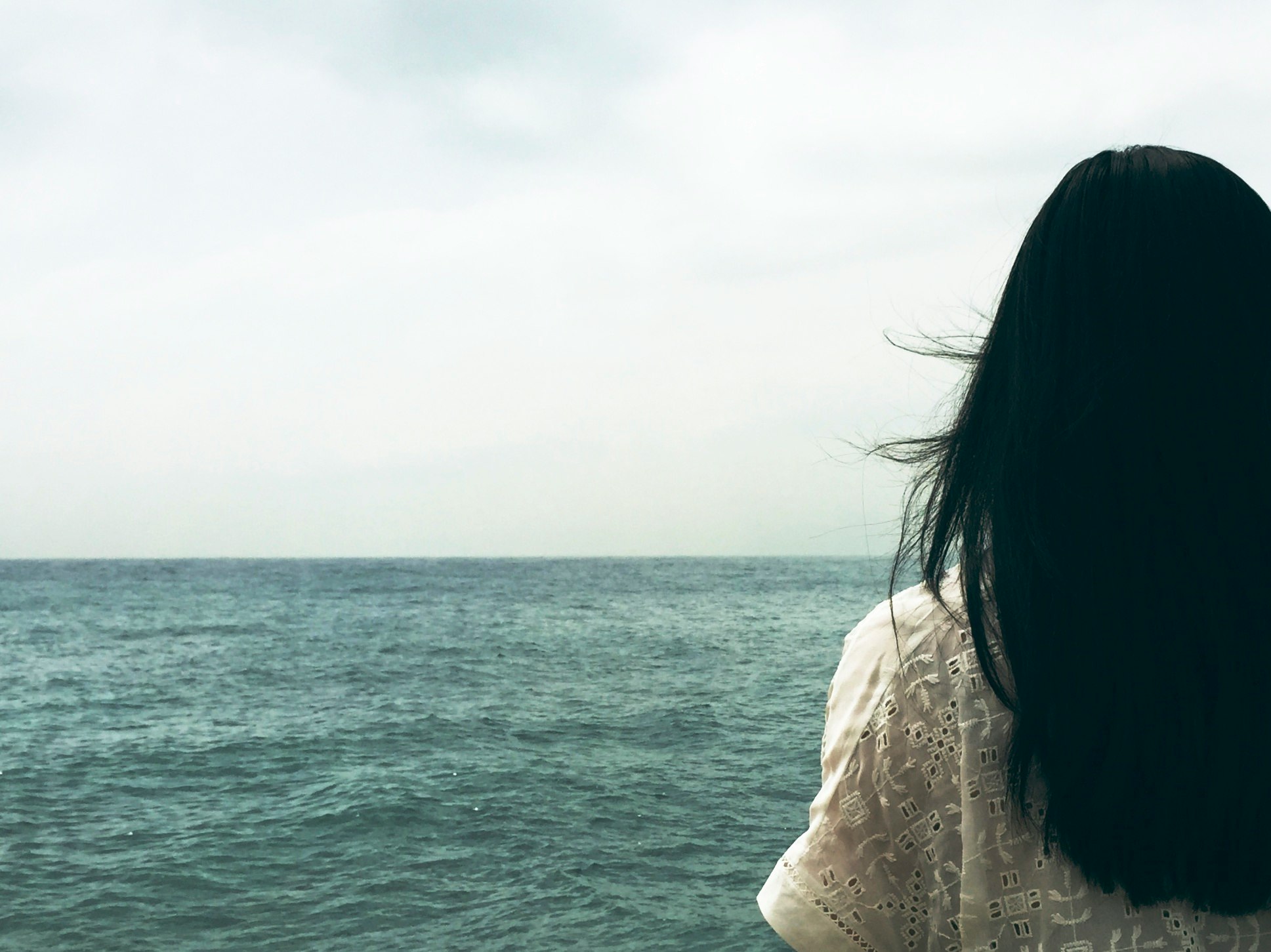 woman facing body of water under cloudy sky